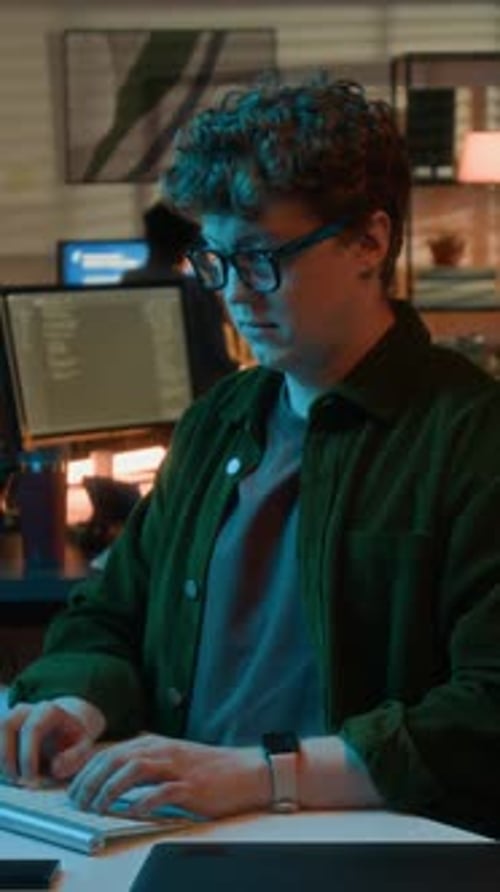 Vertical of Programmer with Glasses Typing on Keyboard in Office at Night