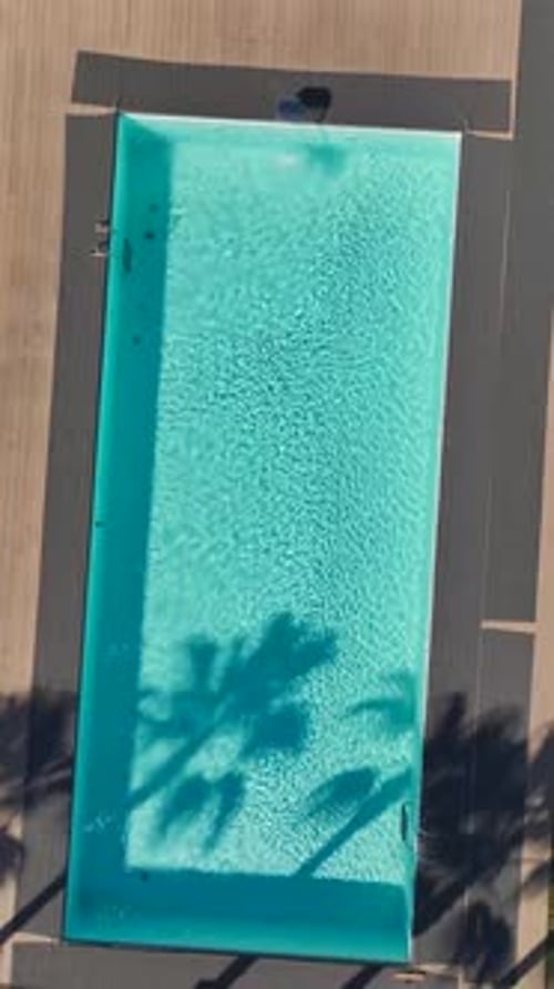 Vertical Video of a Large Pool With Relaxing Chairs and Umbrellas Around It Captured From an Aerial