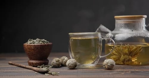 Frisch gebrühter heißer blühender Blumentee wird in eine Glastasse und Tasse aus einer Glasteekanne gegossen