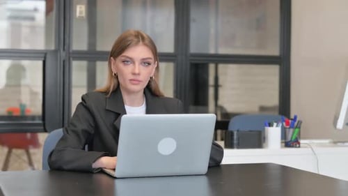Young Businesswoman Looking at Camera while Working on Laptop in Office