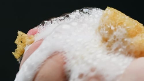 Fingers Squeezing a Soapy Yellow Sponge in Close Up