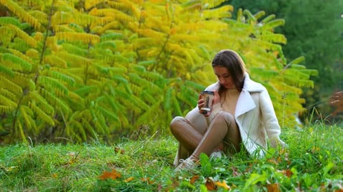 Woman Drinks Coffee in Autumn Park