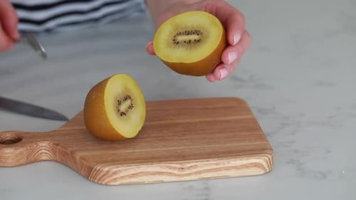 Slicing a Fresh Gold Kiwi Fruit on a Wooden Cutting Board in the Kitchen Area