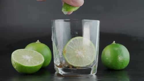 Limette von Hand in ein Glas mit Eis und Zitronenscheiben mit Limetten auf schwarzem Grund pressen