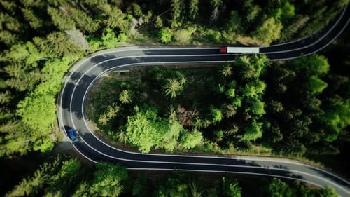 Aerial top view truck and trailer driving down a beautiful country forest road in the mountains.