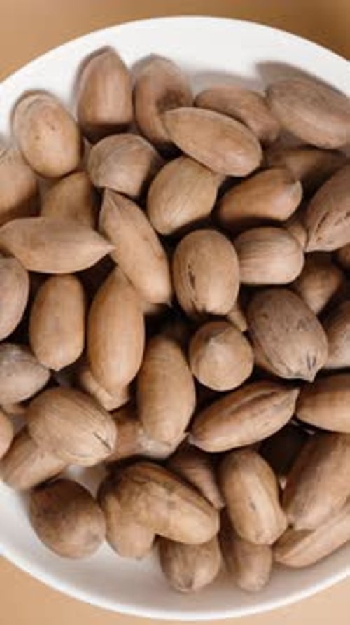 Vertical video. Looping Top-Down View of a White Plate with Pecan Nuts in Shells, Rotating in Place.