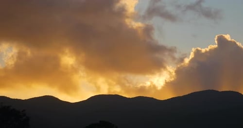 Timelapse of a beautiful summer sunset. Sun going down behind a silhouette of a mountain range. Clou