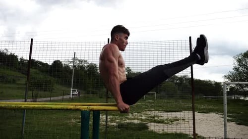 Starker Mann trainiert Bauchmuskeln und hebt die Beine an Parallelstangen auf dem Sportplatz. Junge ohne Hemd
