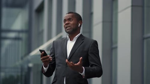 Professioneller afroamerikanischer Geschäftsmann mittleren Alters mit drahtlosen Kopfhörern telefoniert mit