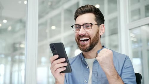 Excited Man Cheering While Looking at Mobile Phone