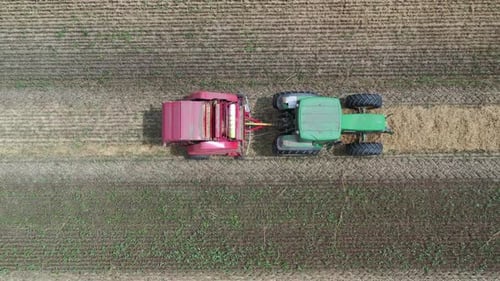 Ein Traktor sammelt Stroh mit einer Anhängerballenmaschine in der