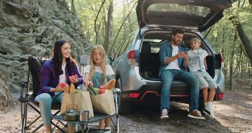 Happy family having weekend picnic outdoors in the forest. Woman and girl preparing food and father