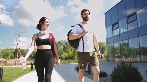 Beautiful and Happy Young Couple with Backpacks and Bottles of Water Walking Together on Street