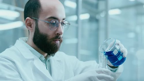 Man in Lab Coat Pours Blue Liquid in Beaker
