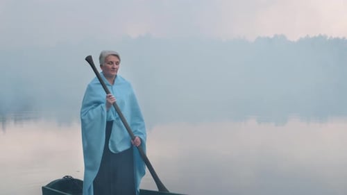 Woman Holding Oar in Rowboat on Foggy Lake