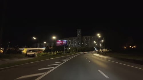 Driving a Car in Summer Night Illuminated City Streets Windshield View