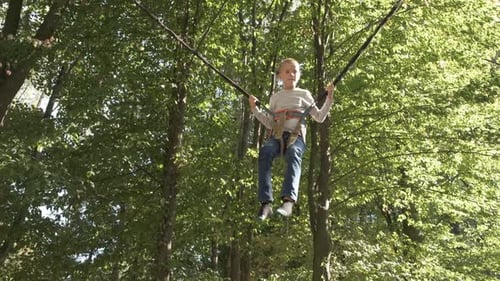 Child Boy Jumping Fastened on a Trampoline in Summer Park