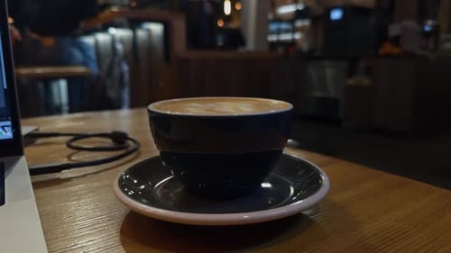 Eine reichhaltige dampfende Tasse Kaffee steht auf einem rustikalen Holztisch in einem gemütlichen und einladenden Café