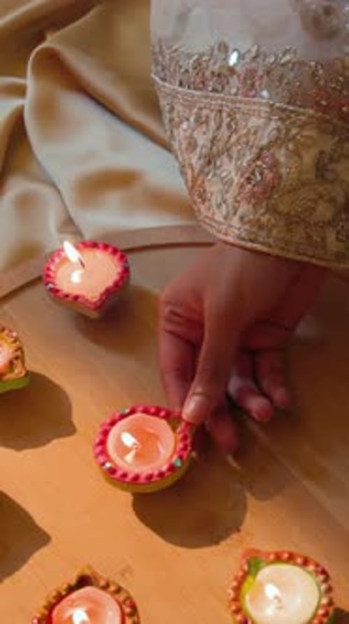 Vídeo vertical: Entrando pela mão direita, manga de lantejoulas, empurrando diyas iluminadas em círculo em um quadro redondo