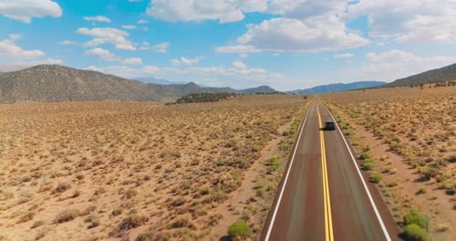 Automobile moving by the two-lane road along the dry sandy landscape. Bare mountains