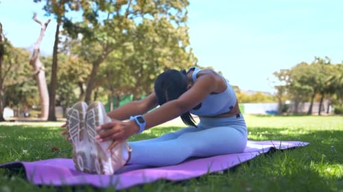 Woman Stretches Hamstrings on Yoga Mat in Park