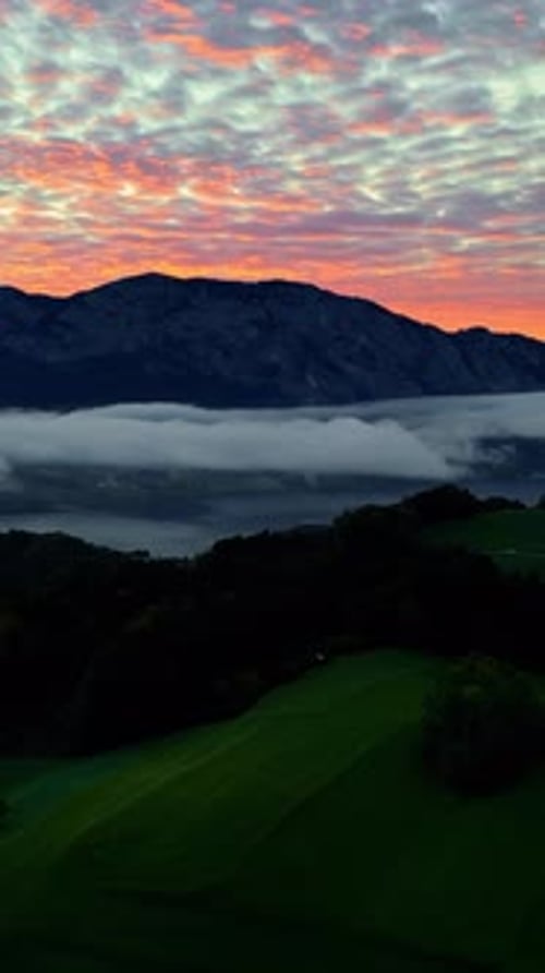 Vista vertical de las siluetas de una montaña con un colorido cielo al atardecer cubierto de densas nubes. Aéreo