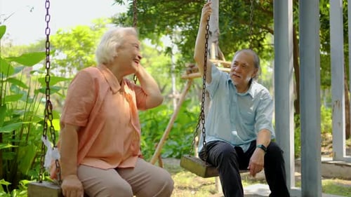 Joyful retired couple savors their holiday by swinging on cozy swings, exchanging stories in a park