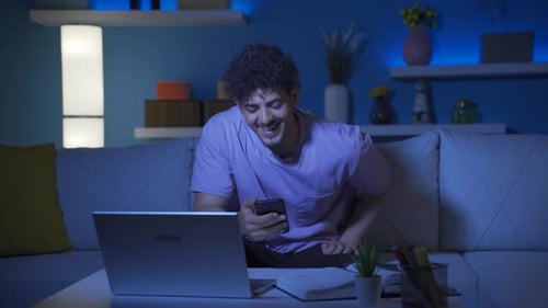 University student chatting on the phone at home at night. He's laughing.