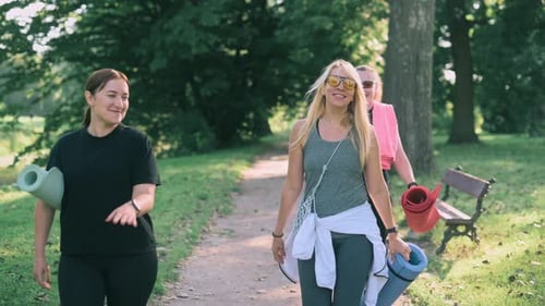 Three women walk in the park with yoga mats
