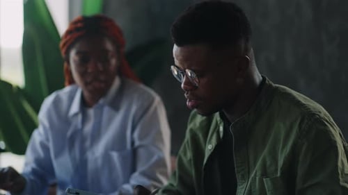 A Man and a Woman of AfricanAmerican Descent are in a Cafe and Conducting a Business Meeting Using a