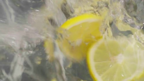 Fresh lemon pieces gracefully fall in water creating gentle splash, close up