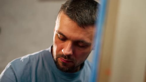 Closeup of a Young Artist in Blue Tshirt in an Art Studio Working on a Painting