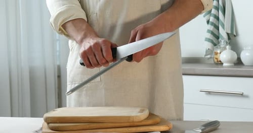 Man sharpening knife with sharpener at beige table indoors, closeup