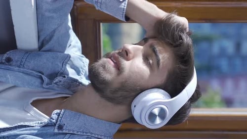 Vertical video of Unhappy man listening to music with headphones.