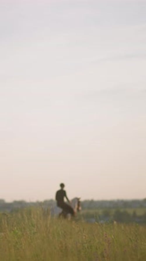 Two Riders on Horseback in a Grassy Field at Sunset