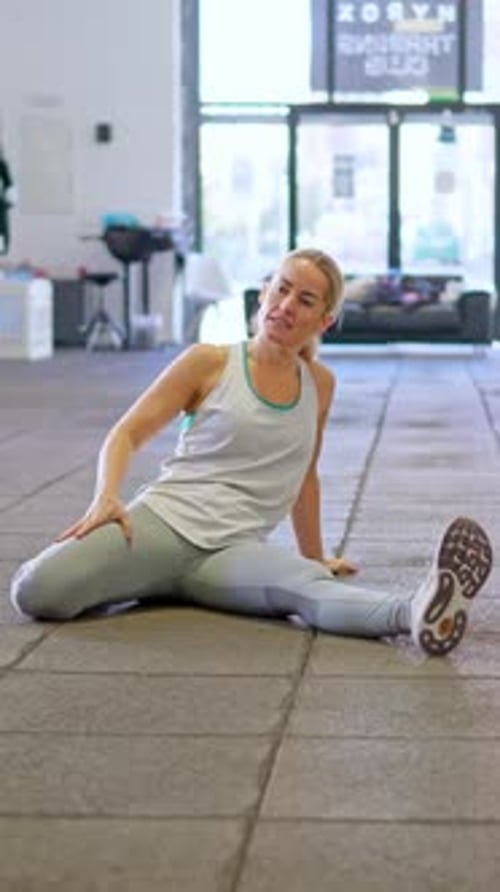 Fit Woman Doing Warm Up Stretching Leg Exercises on the Gym Floor