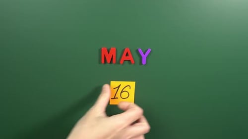 Hand sticking a sticker 16 May calendar day on school board. 16 date of May. Sixteenth day May