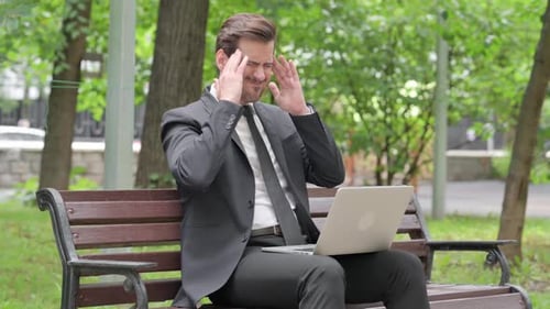 Man on Bench Types on Laptop Experiencing Headache