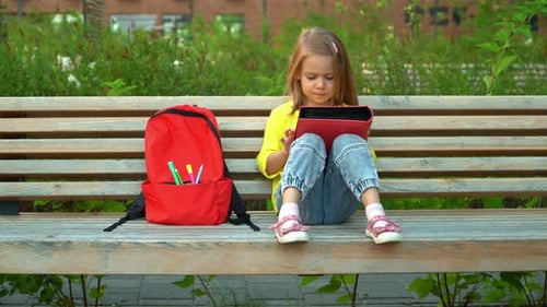 Girl Sits with Backpack in Schoolyard and Reads Book Education and School