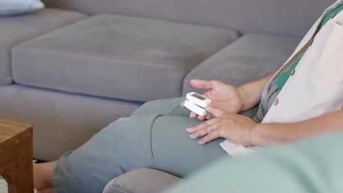 Idoso sentado no sofá, segurando o dispositivo no colo, ajustando e estendendo a mão direita para fora, enfatizando