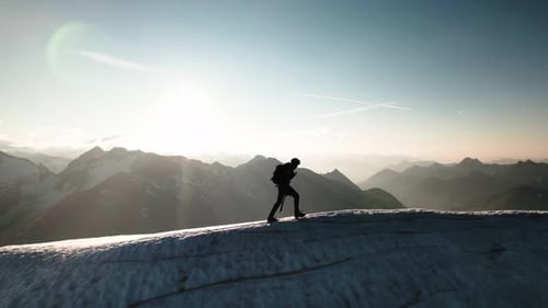 Mountaineer is walking with crampons on the snow and ice covered ridge of a glacier.