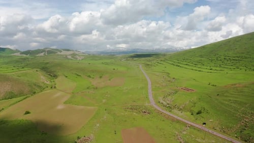 Aerial shot mountain road, cultivated lands, green fields.