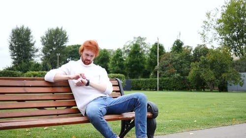 Using Smartwatch Man Sitting in Park on Bench Red Hairs and Beard