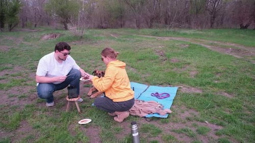Couple Grilling Sausages at Outdoor Picnic With Dog