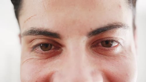 Portrait close up of brown eyes of happy biracial man smiling at home, slow motion