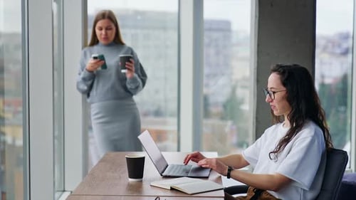 Relaxed atmosphere in the modern office. Brunette woman works on her laptop.