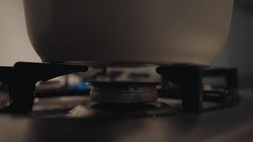 Closeup of Unrecognizable Person Turning Knob of Gas Stove in Kitchen Blue Flame Heating Water in