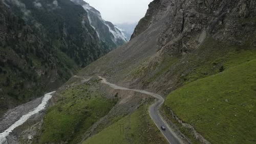 Aerial Drone footage of a black car driving through the curved road in the mountains