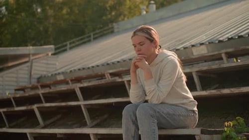 Reflective Woman Sitting on Rustic Stadium Bleachers