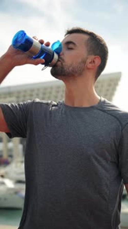 Vertical Young Handsome Sportsman Drinking Energy Water From Bottle While Resting After Run Workout